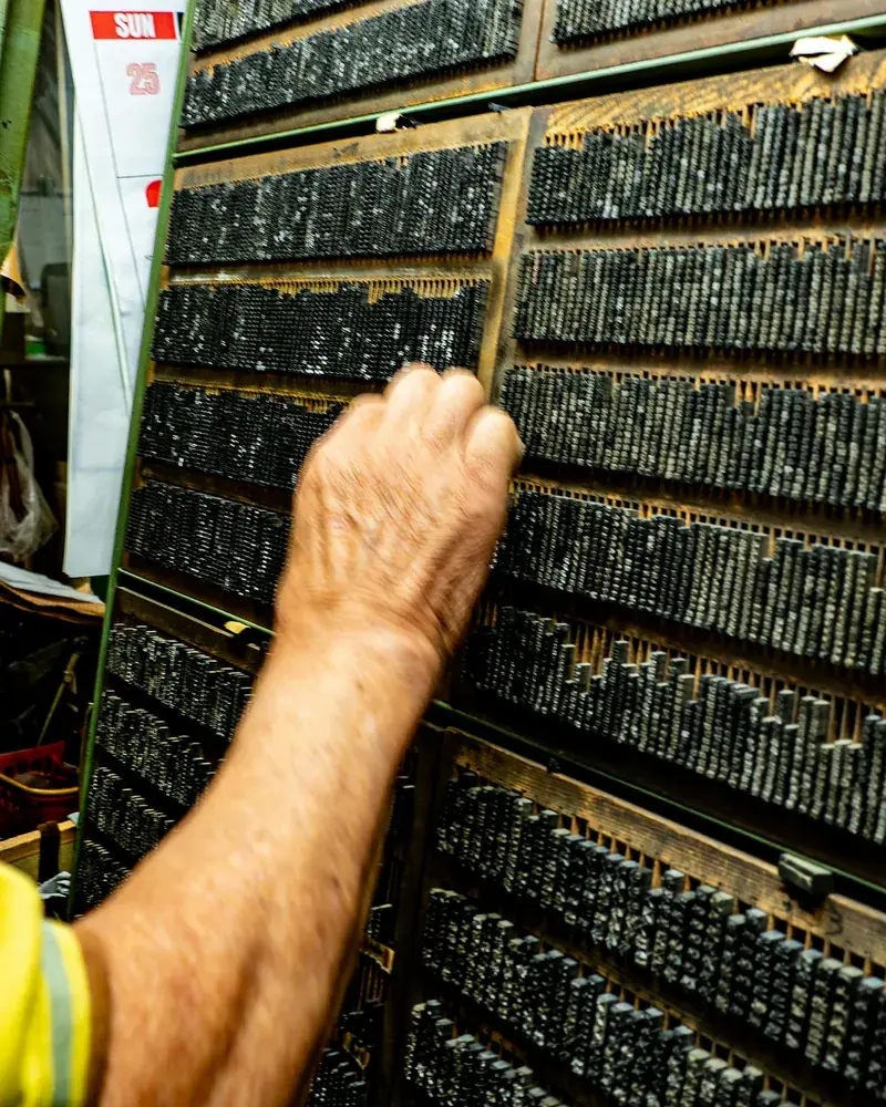 Mano tomando un tipo de plomo de un cajetín de la caja tipográfica